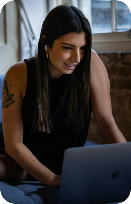 Femme souriante travaillant sur un ordinateur portable, symbolisant la création de sites web sur-mesure et une expérience utilisateur agréable.